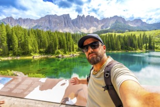 Tourist taking a selfie at lake carezza, with the stunning latemar massif and picturesque dolomites