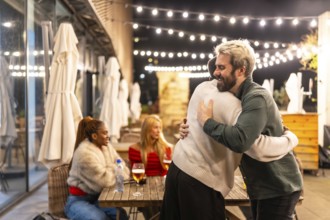 Multi-ethnic friends hugging when arriving at meeting in a bar at night