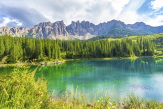Emerald waters reflecting the latemar group and surrounding pine forest under a blue sky with