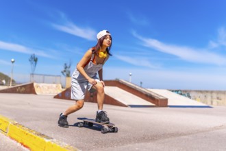 Full length photo of a cool asian young woman practicing in an urban skateboard park