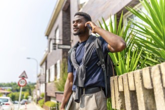 African young businessman talking to the mobile in the city standing holding laptop in a