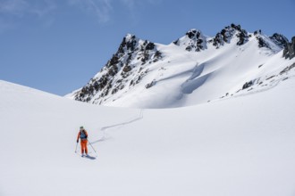 Ski tourer on the descent, minimalist winter landscape, white snow and dark mountains on the