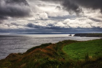 Atmospheric landscape with dark clouds over the sea and lush coastal meadows, Waterford Coast