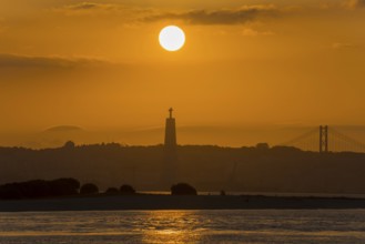 Atmospheric scene with a sunset over a statue and a bridge bathing the water in golden light,