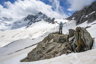 Mountaineer on a rock between snow, raises her arms triumphantly, descending from the summit of