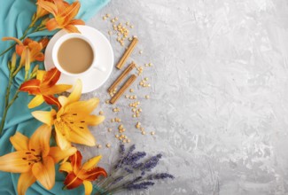 Orange day-lily and lavender flowers and a cup of coffee on a gray concrete background, with blue