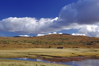 Peaceful lake surrounded by meadows and hills under a blue sky with white clouds, autumn, October,