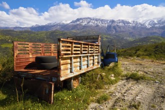 Abandoned rusted lorry in a sunny mountain landscape with snow-capped peaks, wrecked vehicle,