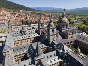 Close-up of a historic monastery with towers, surrounded by a town and mountains in the background,