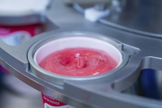 Raspberry ice cream in a cup during the filling process, ice cream production farm ice cream,