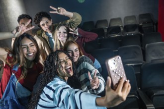Group of cheerful young friends taking selfie at movie theater or disco party, making victory signs