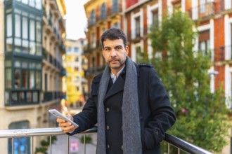 Confident casual businessman using smartphone leaning on a rail in a city viewpoint in winter