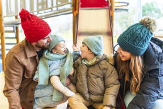 Happy family dressed in warm winter clothing enjoying playful moments together on a playground