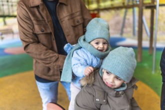 Father holding two joyful children in colorful winter clothes while enjoying playful moments at an