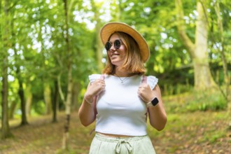 Beauty female caucasian tourist wearing sun hat and sunglasses walking along a green forest in
