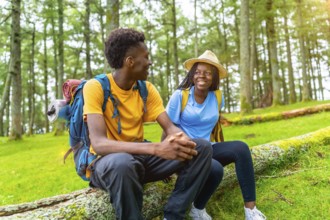 Two male and female african friends resting and chatting during a hiking in the forest