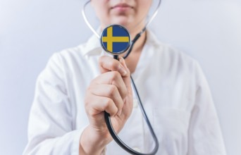 Female doctor holding stethoscope with Swedish flag. National health system of Sweden