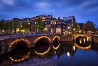 Night view of Amsterdam cityscape with canal, bridge and medieval houses in the evening twilight