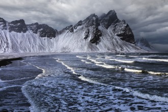 White foamy waves on the beach of Stokkness, behind snowy rocky slopes of Vestrahorn, near Höfn,
