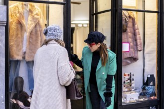 Young blonde girl shopping in the city and served by a shop assistant, looking at shop windows of