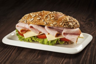 Ham sandwich with lettuce, cheese, tomato on plate on wooden table