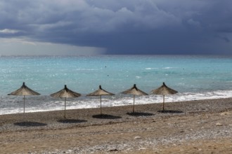 Line of sunshades along the beach with dark storm clouds offshore, Dhermi, Albania, Europe