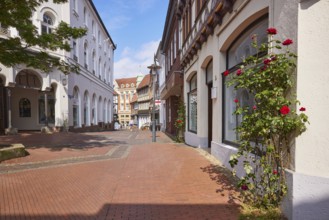 Pedestrian zone of red cobblestones and whitewashed houses with roses (pink) on the facade in the