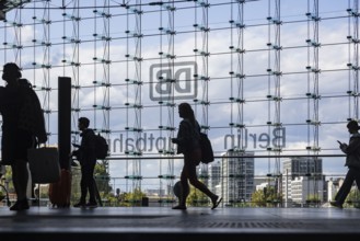 Central station, travellers in front of the glass facade with the logo of Deutsche Bahn AG. Berlin,