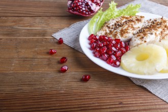 Fried chicken fillets with lettuce, pineapple and pomegranate seeds on brown wooden background,