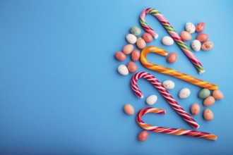 Colorful multicolored candies on a blue background. Christmas cane, chocolate eggs, caramel dragees