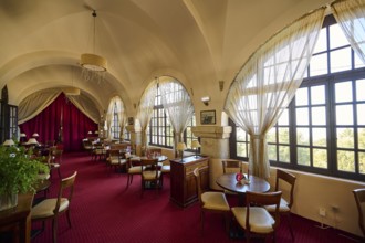 Elegant interior of a restaurant with red carpets, curtains, arched windows and table groups,