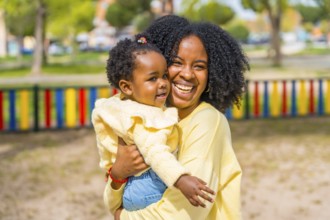 Happy african american mother embracing and holding in arms her little daughter on a park
