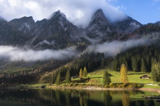 The Vordere Gosausee in autumn with a view of the cloud-covered Gosaukamm. The Seeklausalm in the