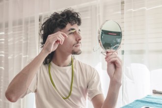 Concentrated young man with curly hair and a goatee meticulously grooming his eyebrows with