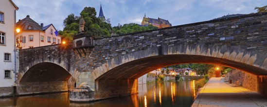 Town view of Vianden with the old stone bridge over the river Our and the castle in the evening,