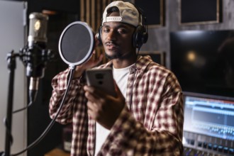 Young man recording vocals for new hit album in professional music studio, using pop filter and
