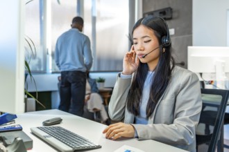 Asian customer service representative working with headset and computer in bright coworking office