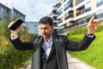 Happy businessman dancing celebrating while holding mobile phone outdoors int he city in a sunny