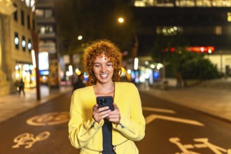 Frontal view of a happy casual woman using phone walking along the city at night