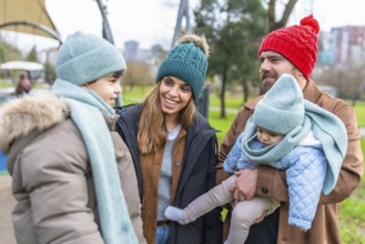 Smiling family wearing winter clothes spending time together at the playground on a cold day