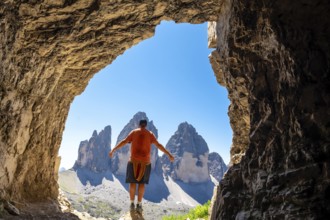 Hiker enjoying the breathtaking view of the tre cime di lavaredo from inside a Tre Cime Cave in the