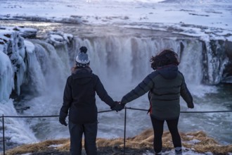 Two people are standing on a ledge looking at a waterfall