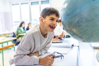Happy student with down syndrome smiling while exploring a globe in geography class, showcasing