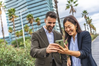 Chinese and caucasian business people laughing while looking at the mobile in the city