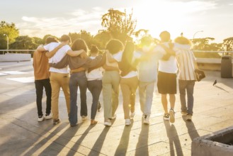 Rear view of friends embracing walking together along the city during sunset