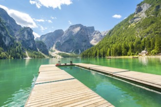 Wooden pier reflecting in the emerald waters of lake braies, surrounded by the dolomites on a sunny
