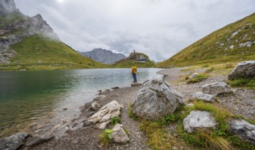 Mountaineer in yellow jacket at the mountain lake, view over the Wolayersee lake to the alpine club