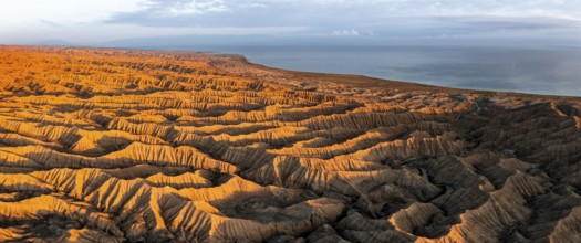 Landscape of eroded hills, badlands at sunset, Lake Issyk Kul in the background, aerial view,