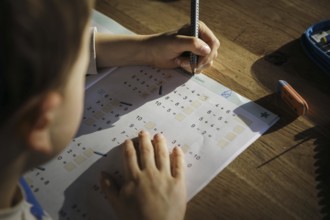 A six-year-old boy does first-grade maths homework at home in a workbook. Berlin, 13.03.2024