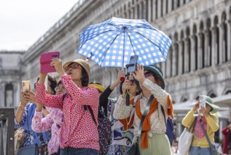 Tourists from Asia with mobile phones and parasols taking photos. Souvenir photo of St Mark's